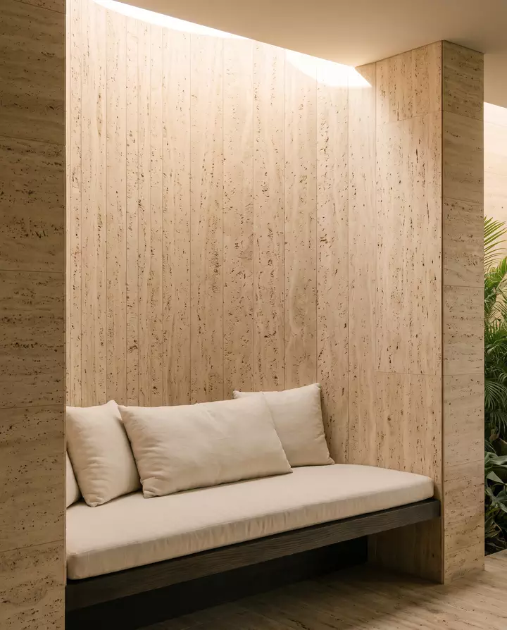 A cushioned bench in a travertine alcove under a skylight